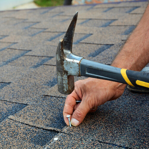 a worker nailing down an asphalt shingle